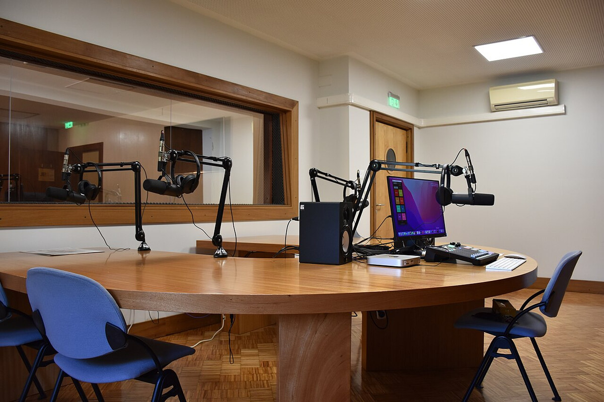 Un estudio de podcast profesional con micrófonos de boom y ventana a la sala de control